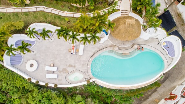 Vista aérea de un resort con una piscina central, áreas de descanso y palmeras.