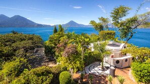 Un jardin avec un sentier circulaire, un petit bâtiment surmonté d’un dôme, et une vue sur une montagne et un lac.