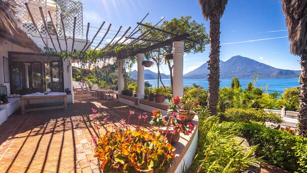 Une terrasse agrémentée d’une pergola, de plantes en pot et offrant une vue sur la montagne et la mer.