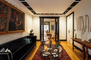 A modern living room with a black sofa, a glass coffee table with candles, and a large floral painting on the wall.