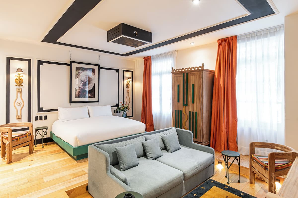 Une chambre d’hôtel moderne avec un grand lit, un canapé gris, des meubles en bois et un plafond doté d’un système de climatisation intégré.