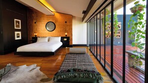 Une chambre moderne avec un grand lit, un plancher en bois et une vue sur un bâtiment aux toits rouges, visible à travers de grandes fenêtres.