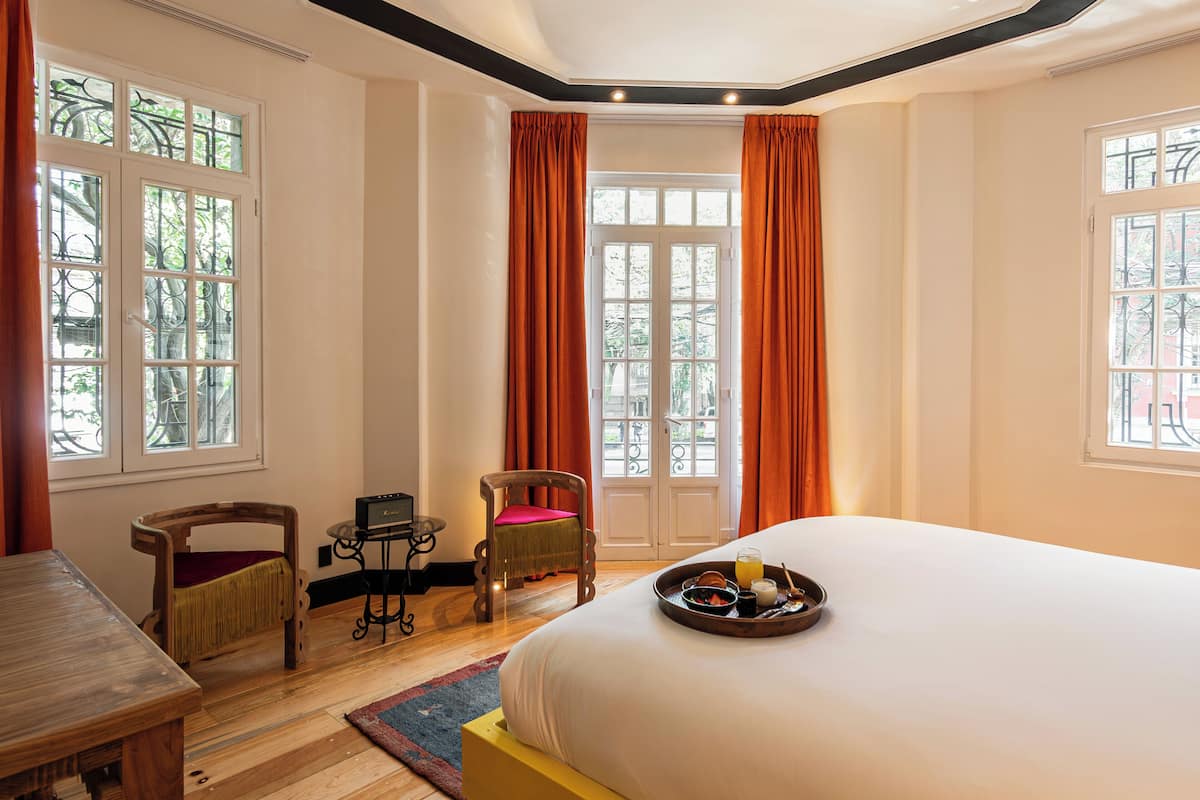 Une chambre d’hôtel avec un grand lit, deux chaises, une petite table et un plateau contenant des articles pour le petit-déjeuner.