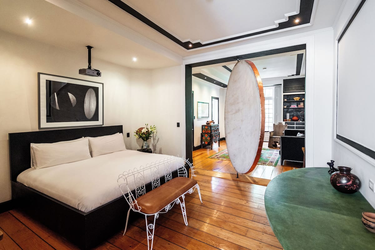 Une chambre moderne avec un grand lit, un banc, un projecteur et un pouf vert.