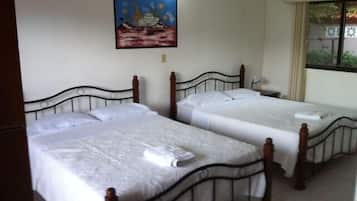 A hotel room with two single beds, a painting on the wall, and a window with a view of greenery.