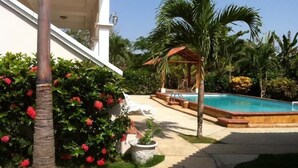 A pool area with a pergola, palm trees, and a white building.