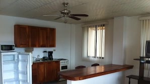 A compact kitchen with wooden cabinets, a microwave, a refrigerator, a stove, and a bar area.