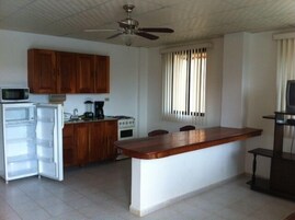 Una cocina compacta con armarios de madera, microondas, refrigerador, estufa y una zona de bar.