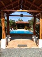 Un área de piscina cubierta con un pérgola de madera, una piscina y vista a un edificio al fondo.