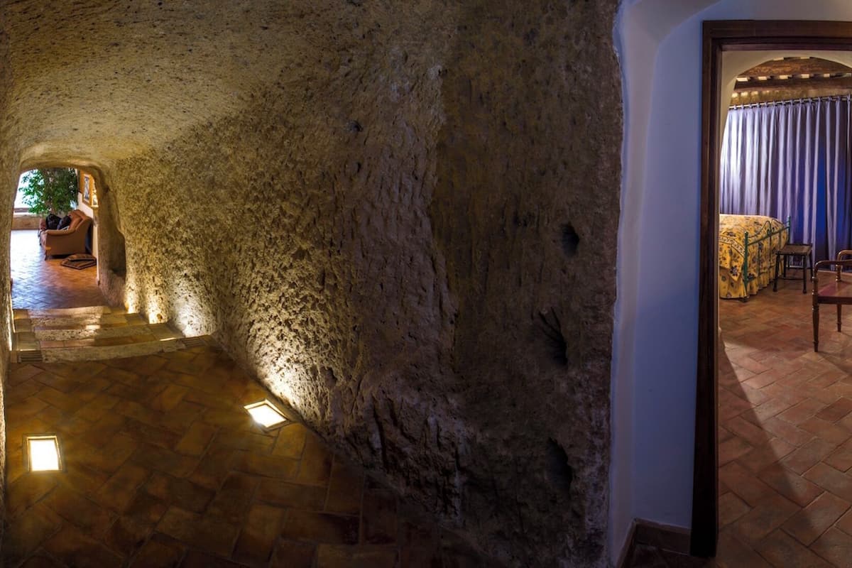 Un pasillo con paredes de piedra que conduce a un dormitorio con cama, cortinas y una silla de madera.