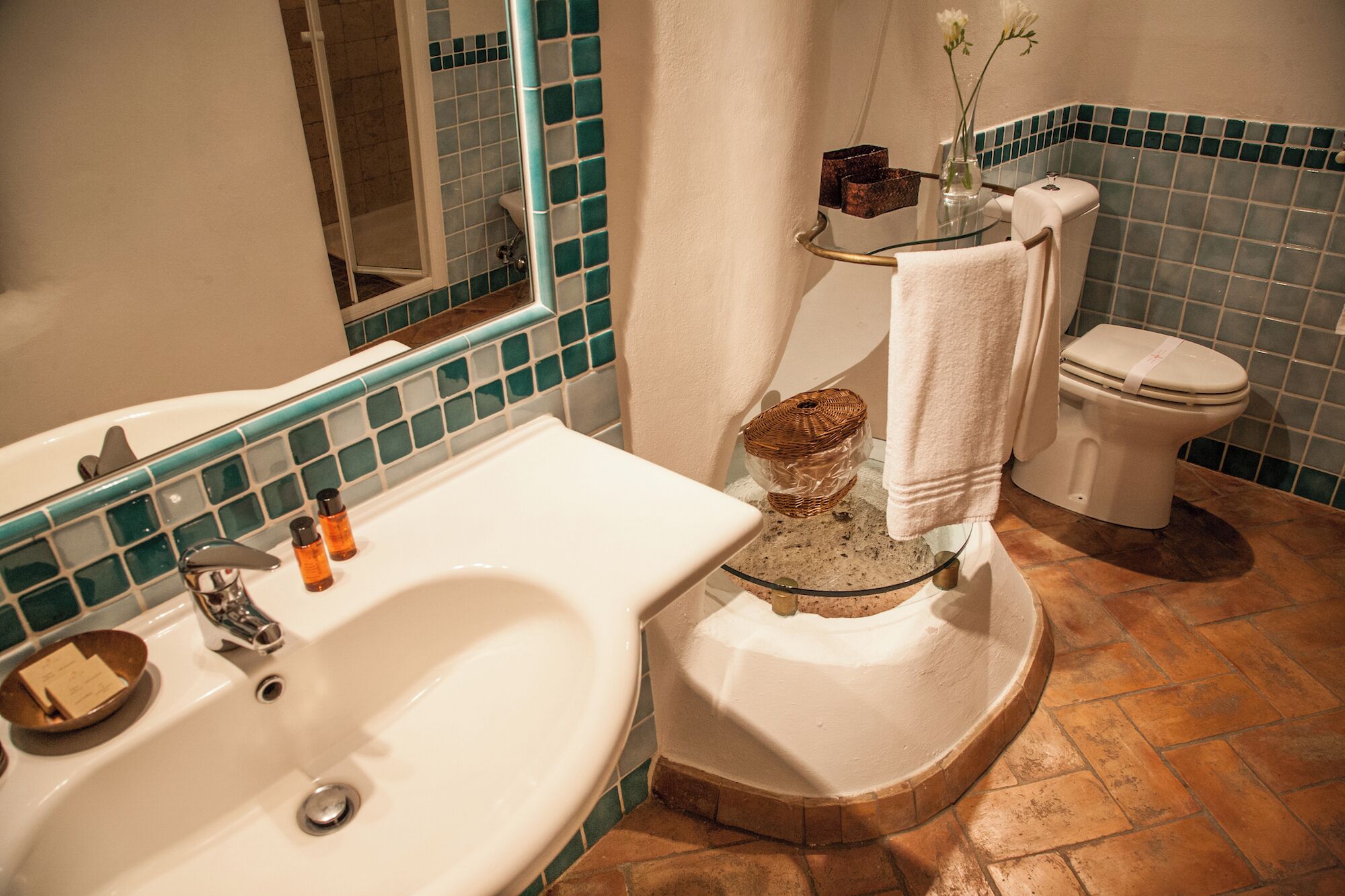 Une salle de bain équipée d’un lavabo, d’un miroir, de toilettes et d’une petite étagère où sont rangés les articles de toilette.