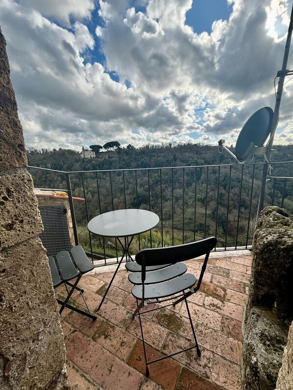 A balcony with a round table and two chairs, overlooking a scenic landscape with a castle in the distance.