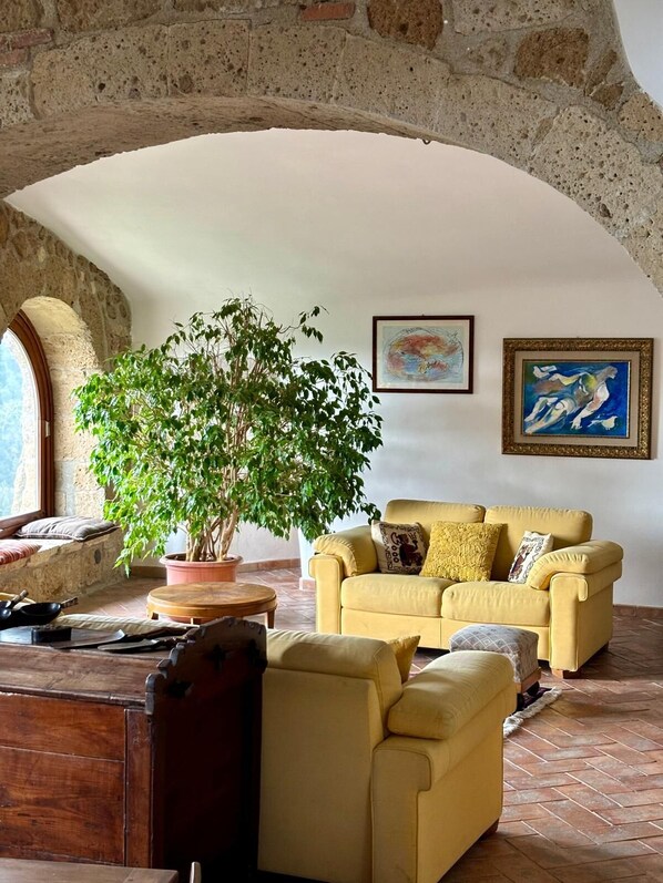 Un salón acogedor con un sofá amarillo, una planta grande en maceta y un techo rústico de piedra.