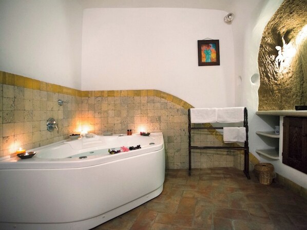 A bathroom with a large bathtub, a towel rack, and a shelf with toiletries. - La Casa degli Archi (Pitigliano)