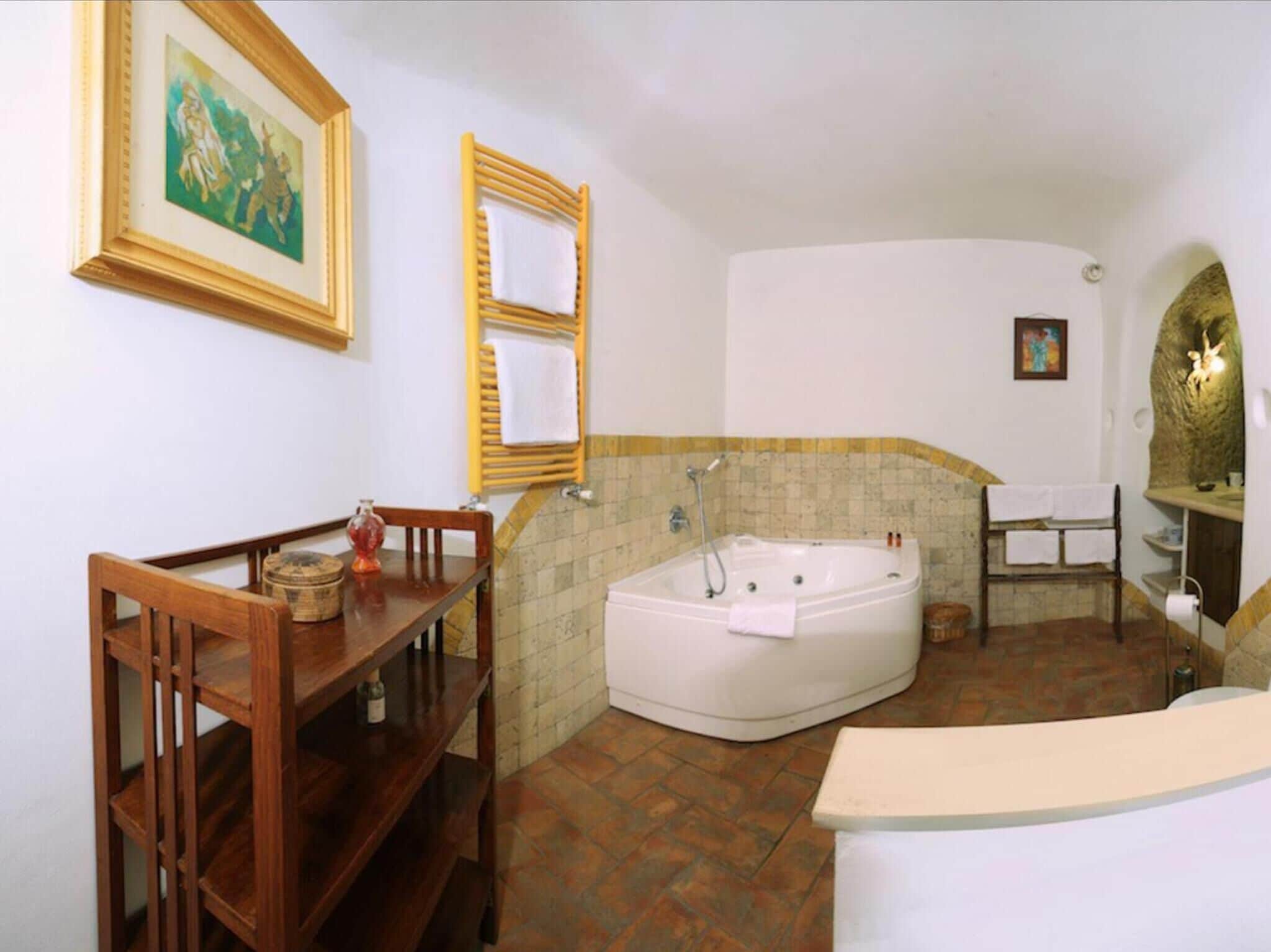 Un bagno con una vasca, una sedia di legno, un piccolo tavolo con una bottiglia e un quadro appeso al muro.