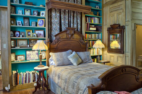 A bedroom with a four-poster bed, a bookshelf, and a mirror.