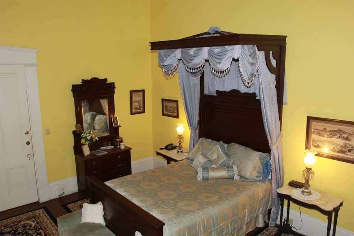 Un dormitorio con cama con dosel, una mesita de noche con lámpara, un tocador con espejo y cuadros en la pared.