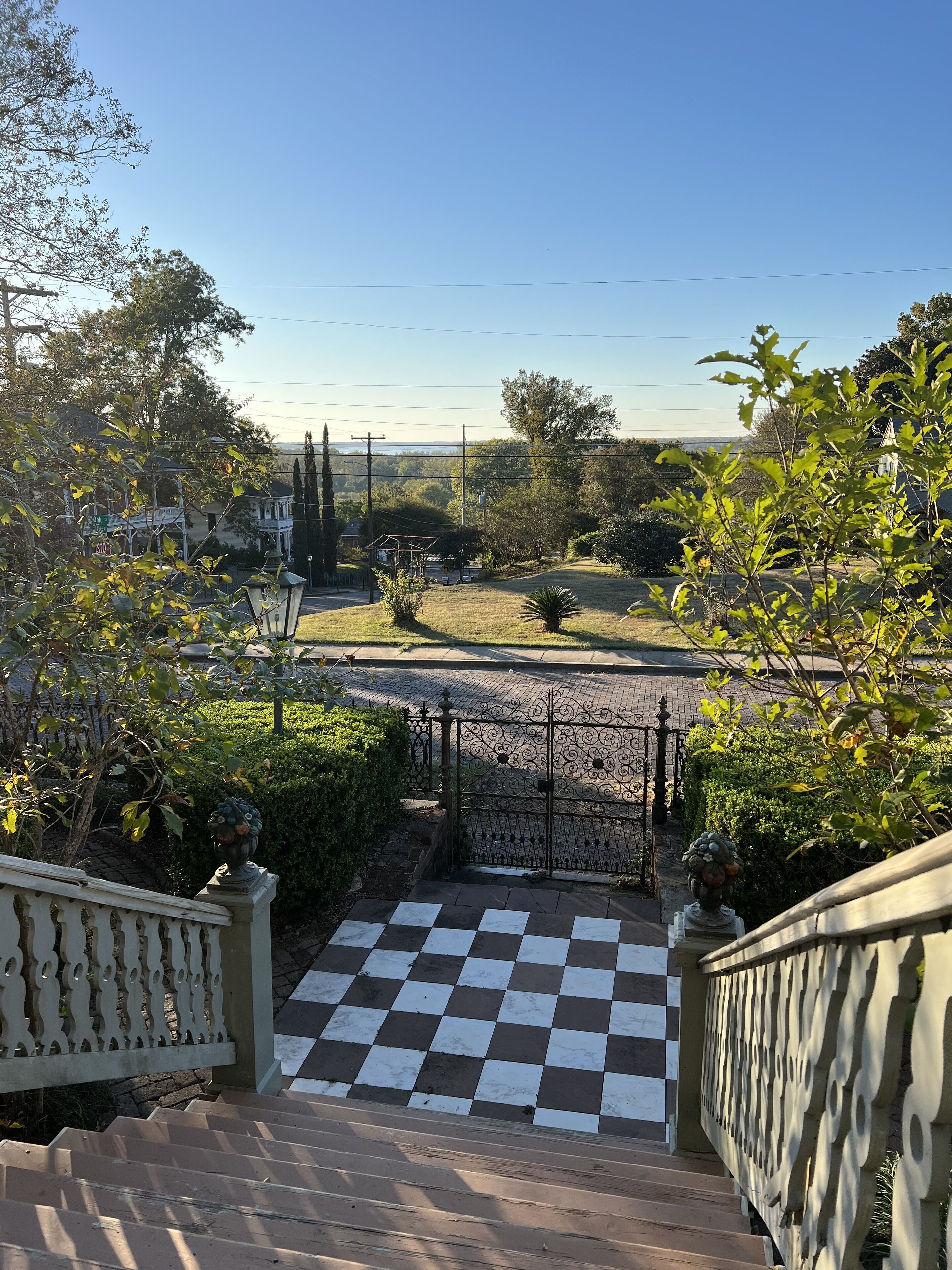 Un espace extérieur à carreaux, agrémenté d’une porte, entouré de verdure et offrant une vue sur une route et un paysage lointain.