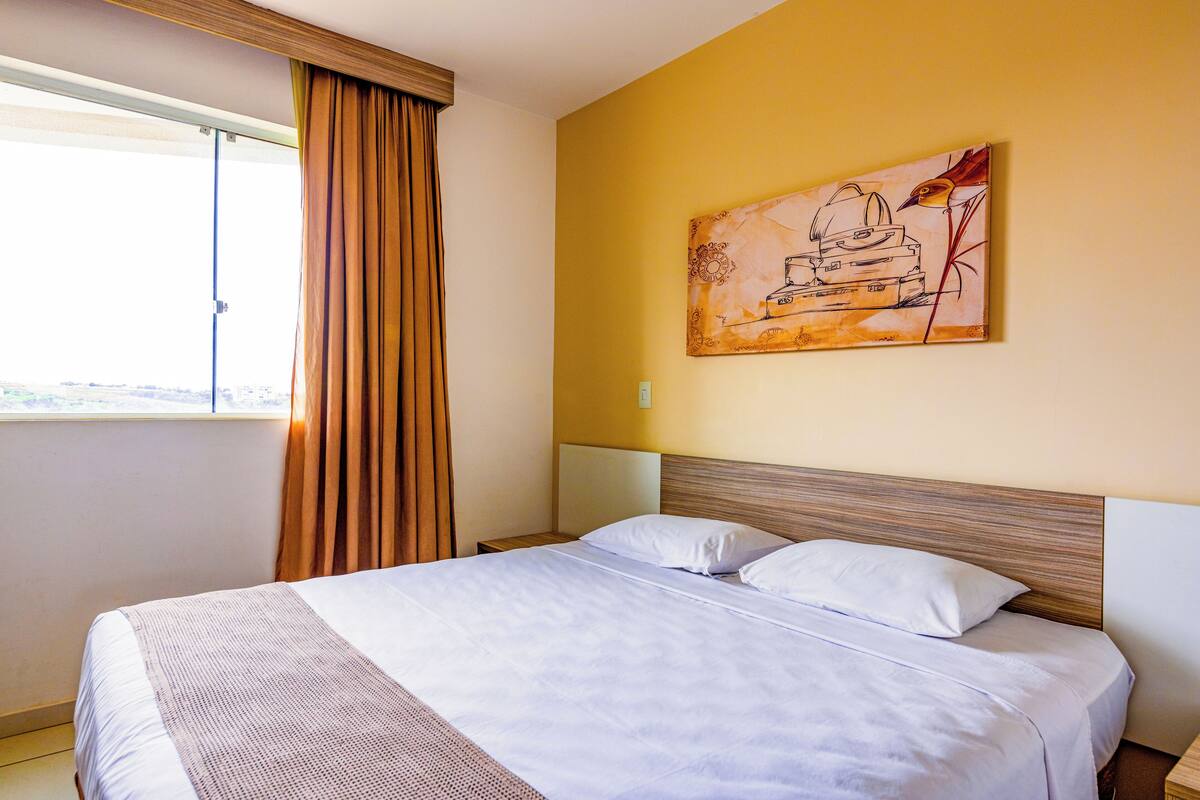 A hotel room with a large bed, a window with curtains, and a painting on the wall.