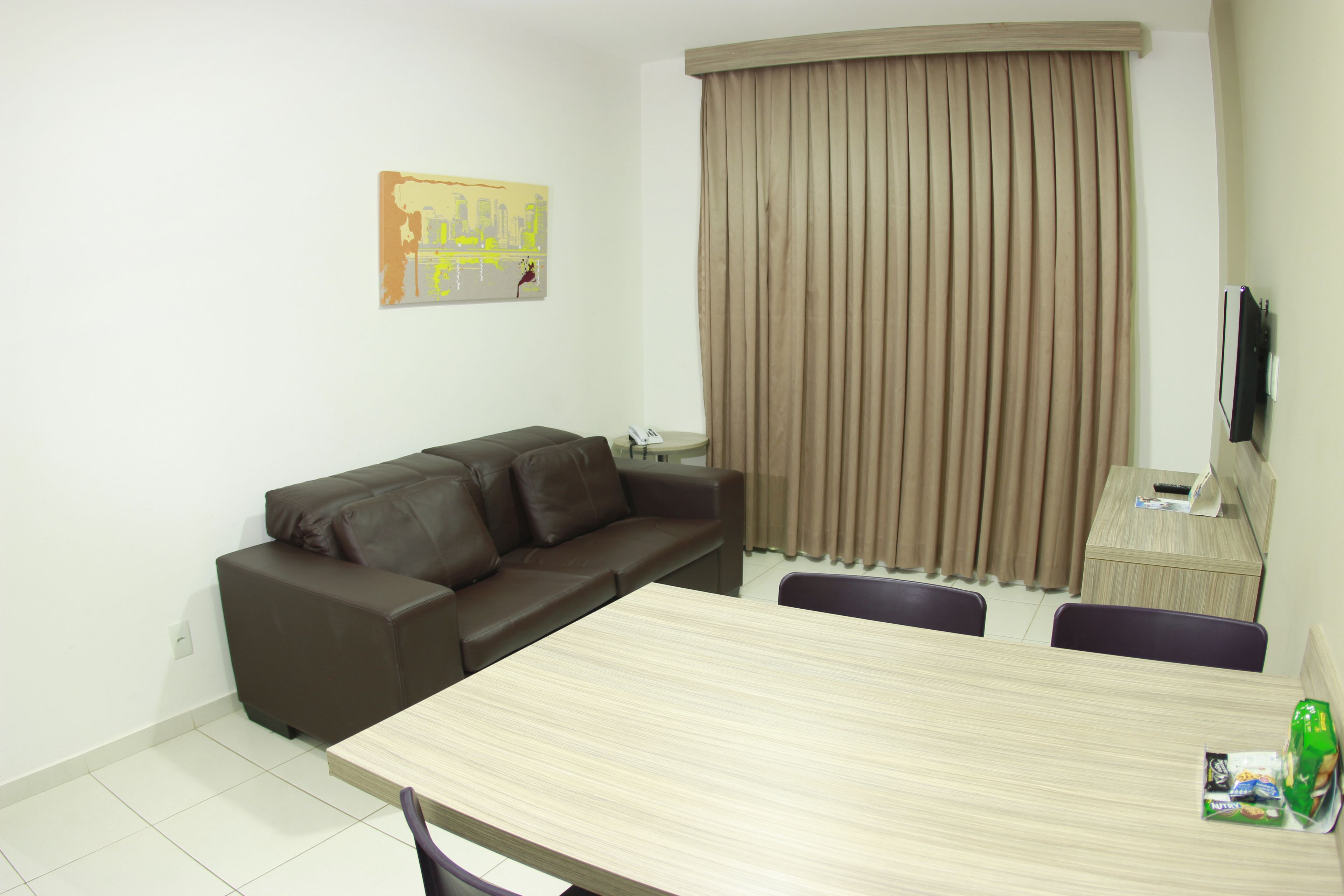 A modern living room with a brown leather sofa, a wooden dining table, and a television mounted on the wall.
