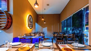 A restaurant with multiple tables set for dining, a large window offering a view of the outside, and a wall-mounted sign with the restaurant's name.