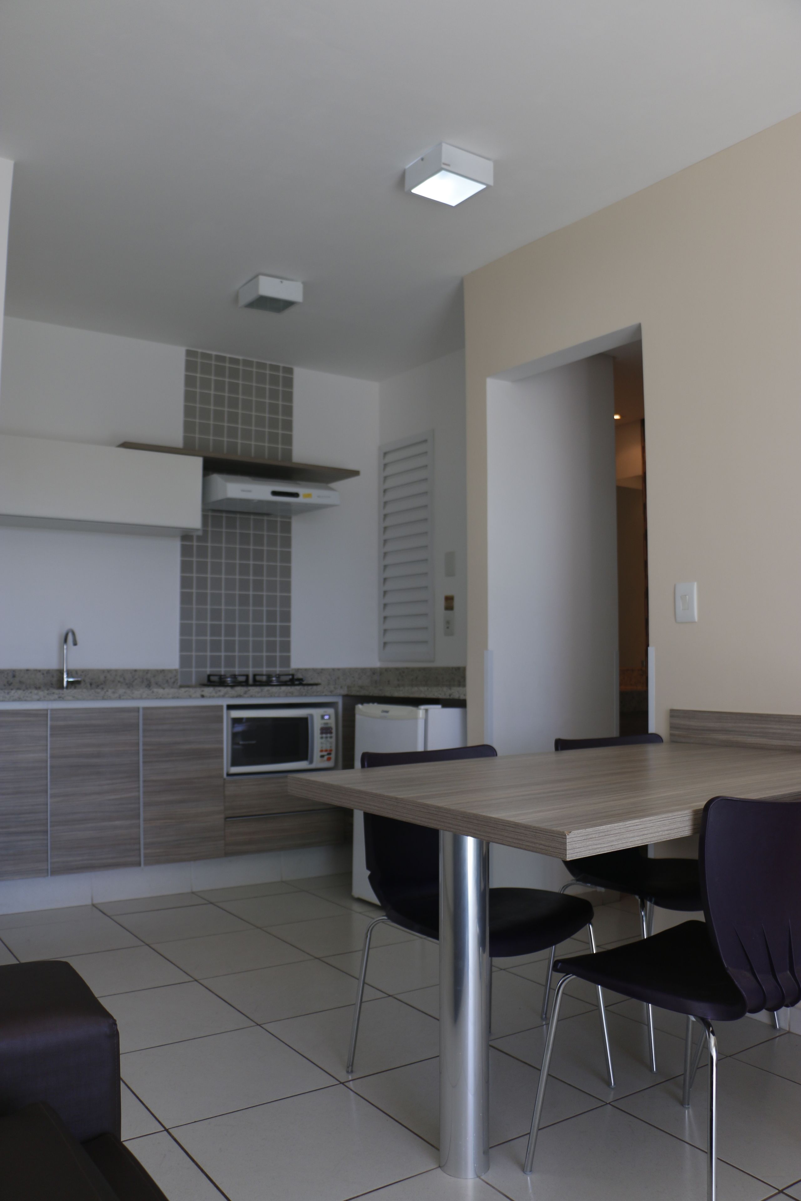 A modern kitchen with a dining area, featuring a built-in microwave, grey cabinets, and a wooden dining table with chairs.