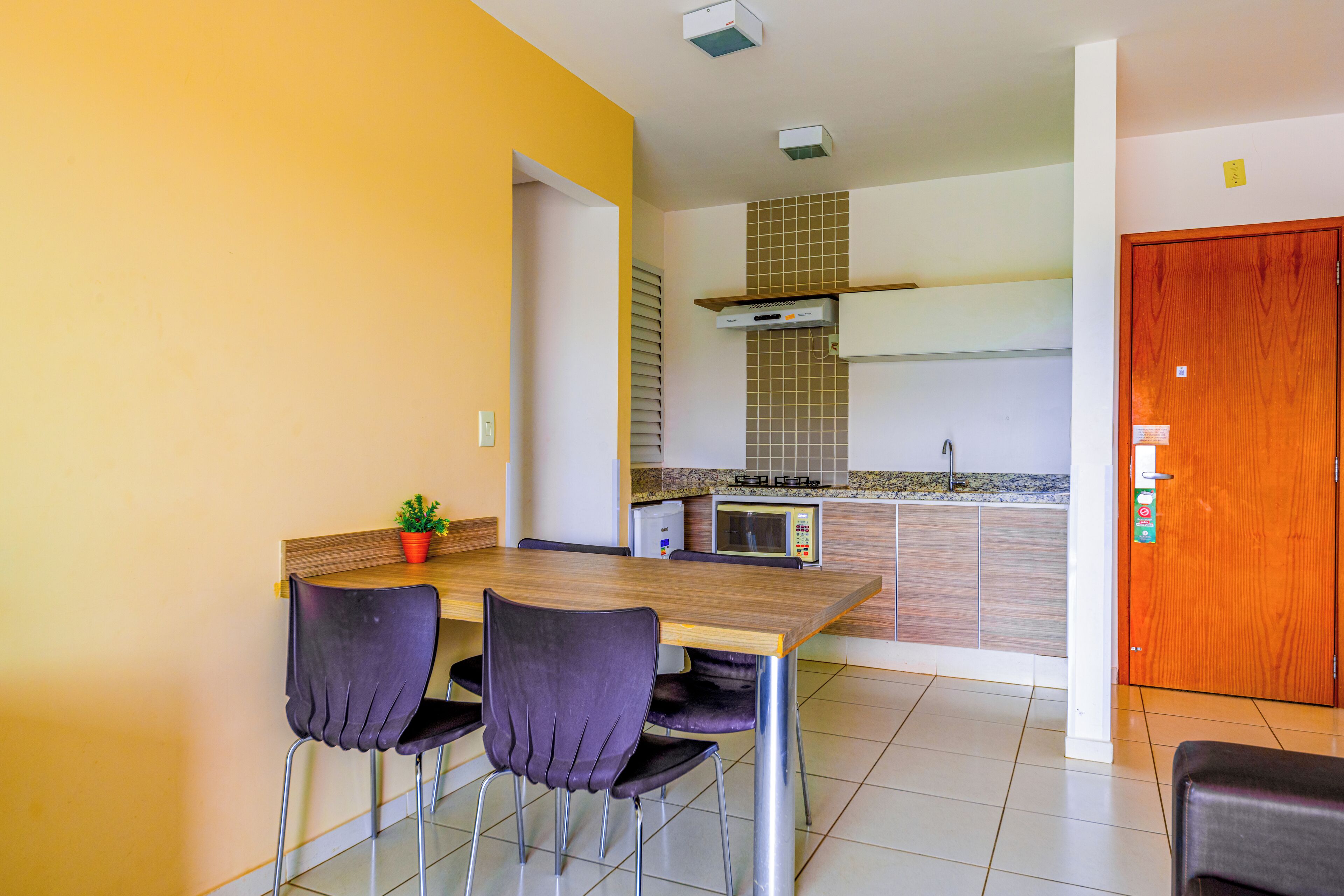 Uma cozinha compacta com mesa, cadeiras, micro-ondas e fogão.