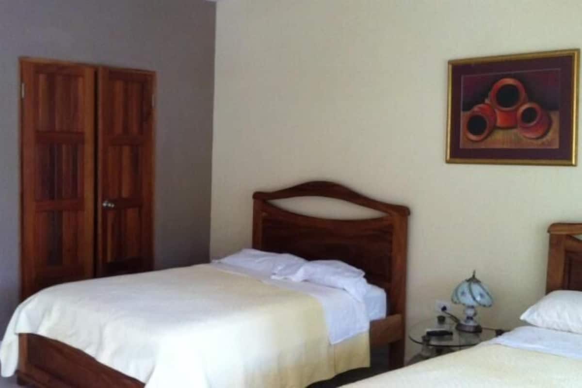 A bedroom with two beds, wooden wardrobe, and a painting on the wall.
