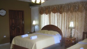 Habitación de hotel con cama doble, dos mesitas de noche con lámparas, un armario de madera y un reloj de pared.