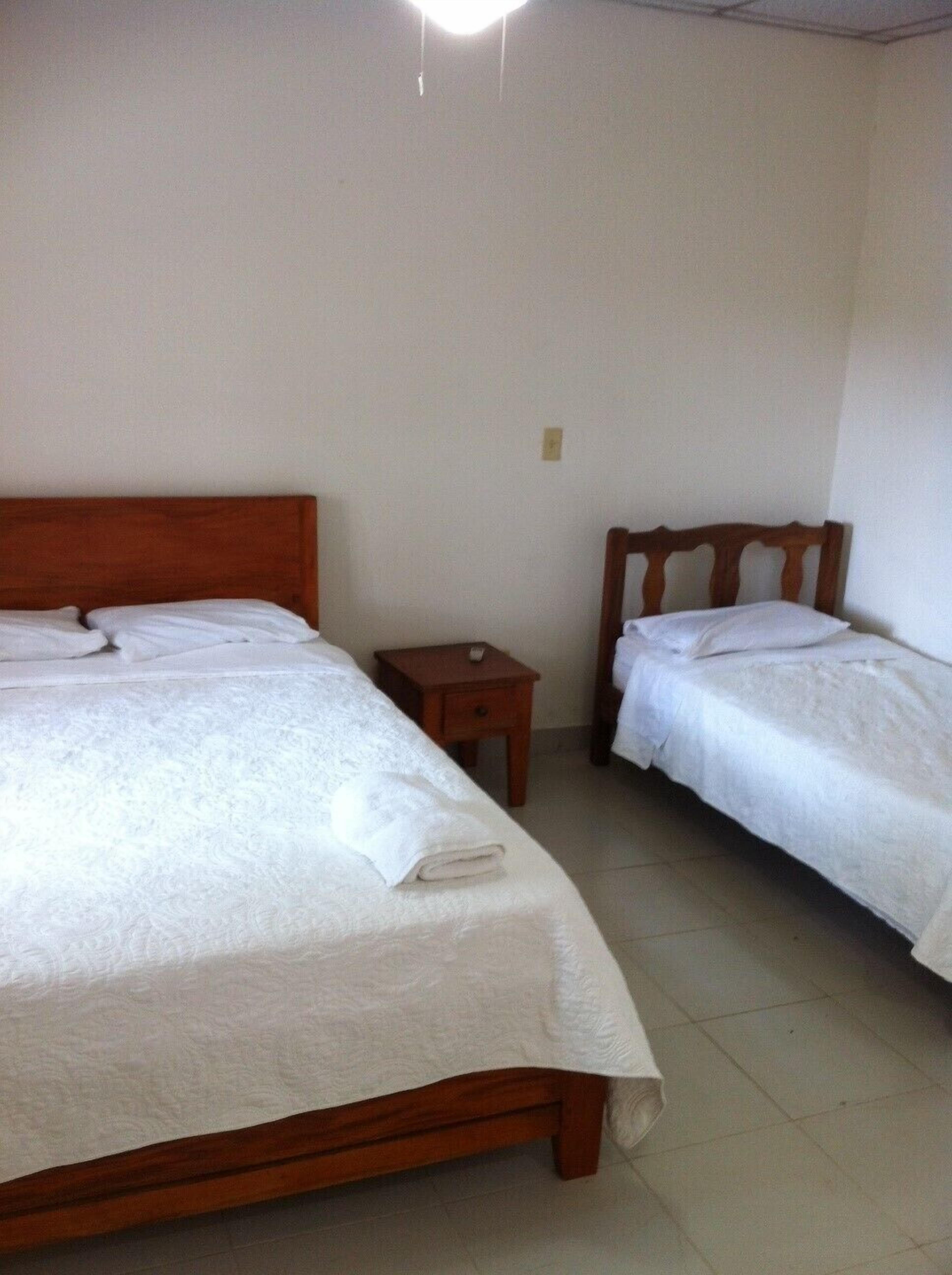 Una habitación con dos camas individuales, cada una con cabecero de madera, una mesita de noche pequeña y una colcha blanca.