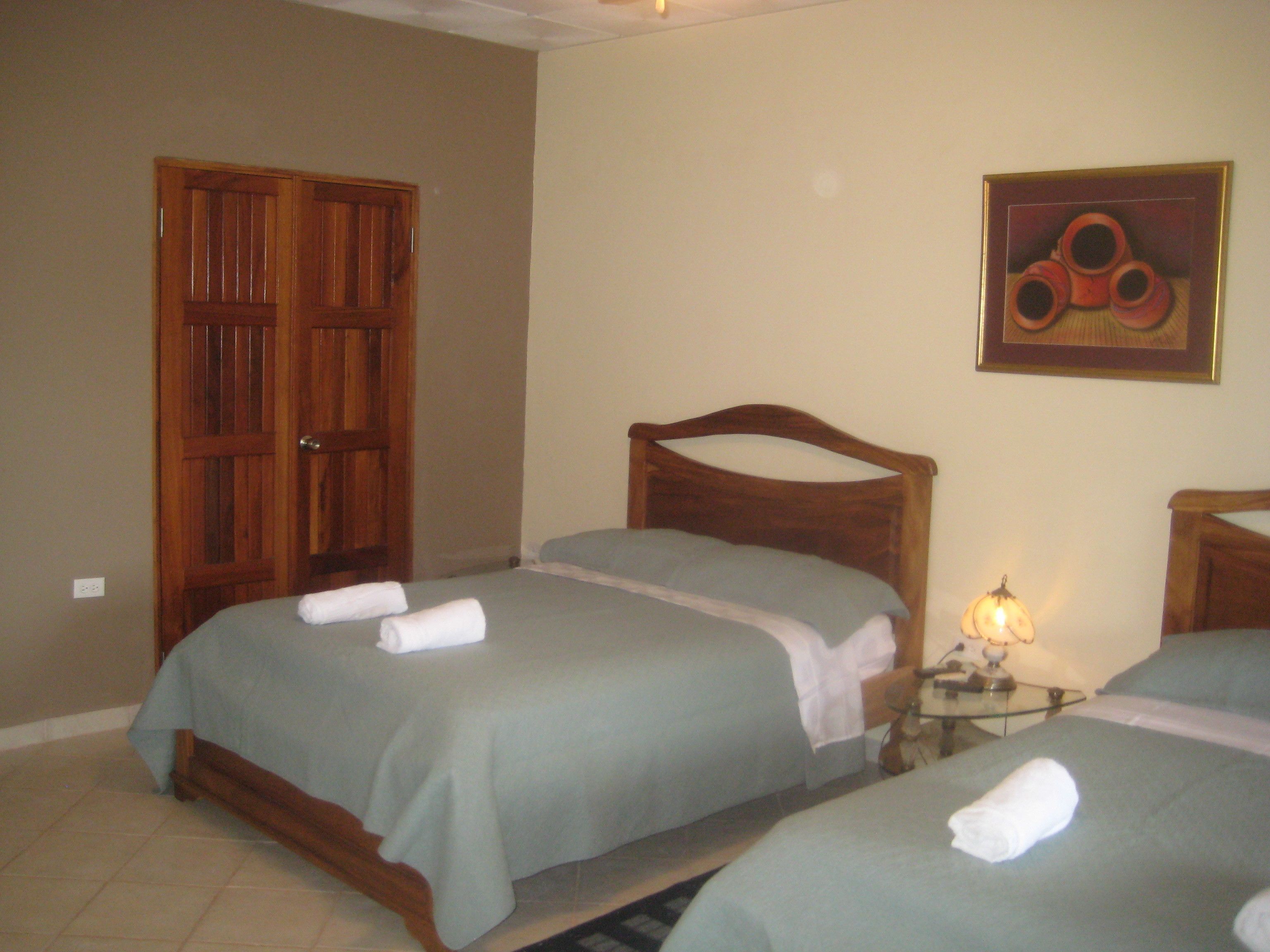 A hotel room with two beds, wooden headboards, a nightstand with a lamp, and a door.
