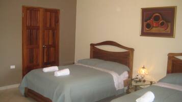 A hotel room with two beds, wooden headboards, a nightstand with a lamp, and a door.