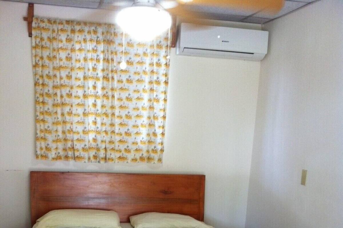 A single-bed room with a wooden headboard, a green bedspread, two pillows, and two folded white towels on the bed.