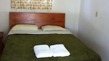 Una cama individual con cabecera de madera, una colcha verde y dos toallas blancas sobre la cama.