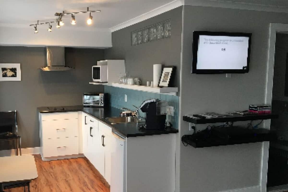 A modern kitchen with white cabinets, a microwave, and a coffee maker. There is a TV mounted on the wall and a small dining area with a table and chairs.