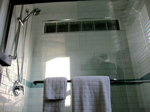A bathroom with white tiled walls, a glass shower enclosure, and two towels hanging on a towel rack.