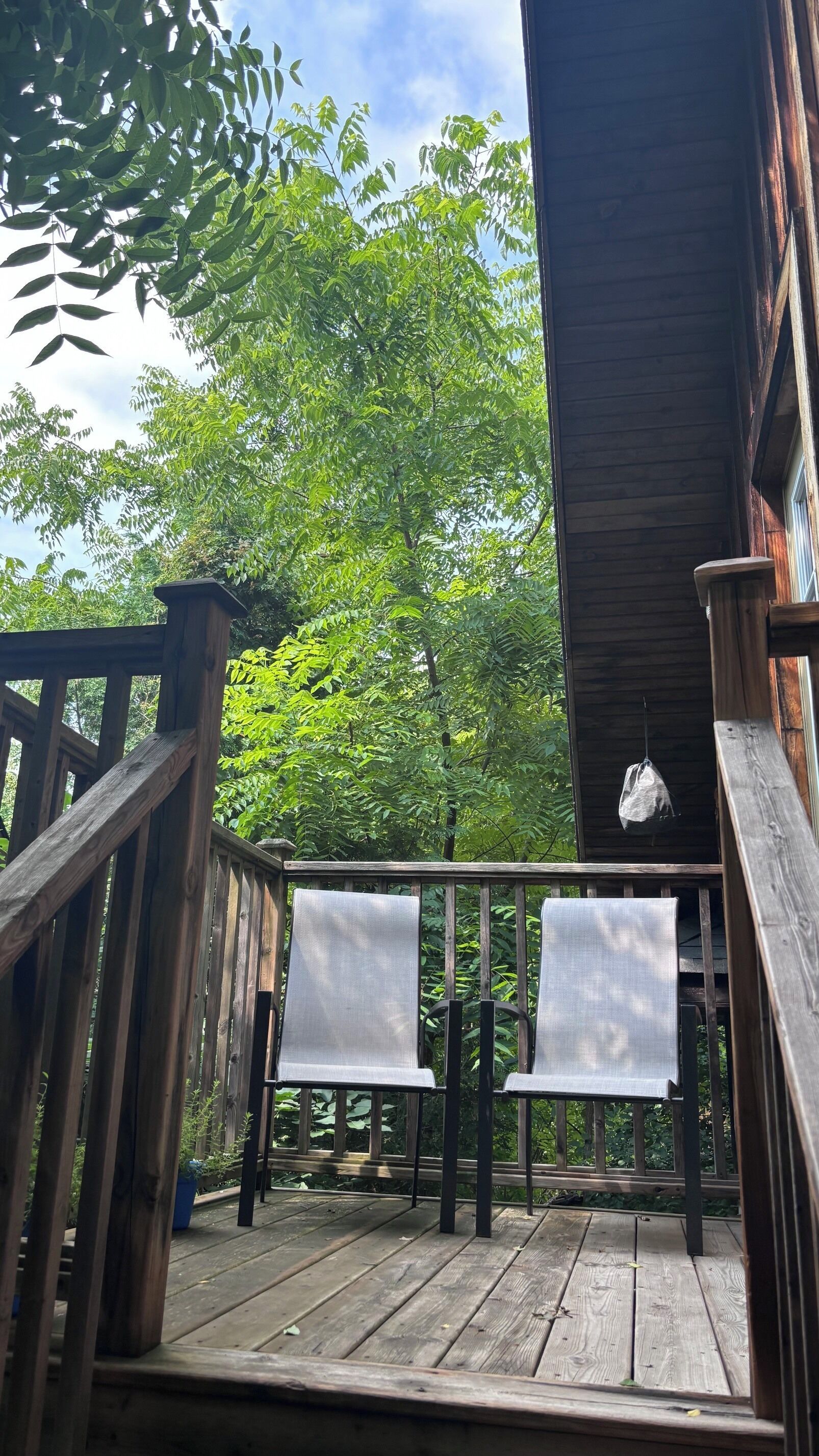 A wooden deck with two chairs and a hanging bag, overlooking a lush green area.