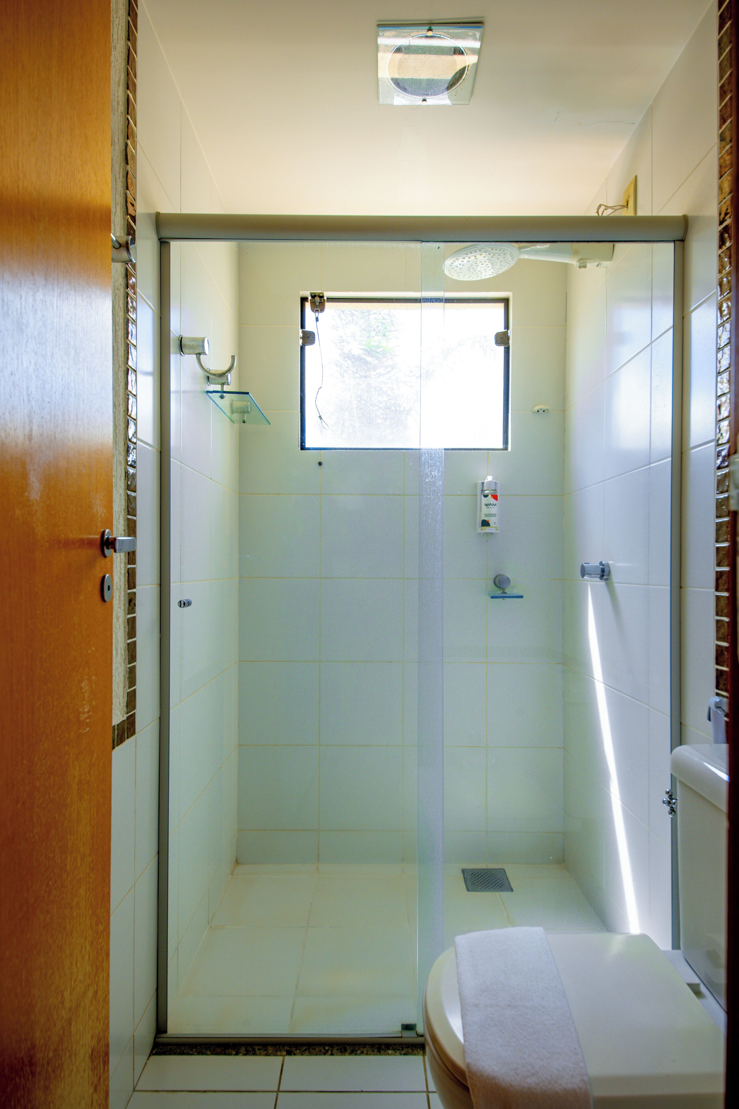 A bathroom with a glass-enclosed shower, a toilet, and a small window.