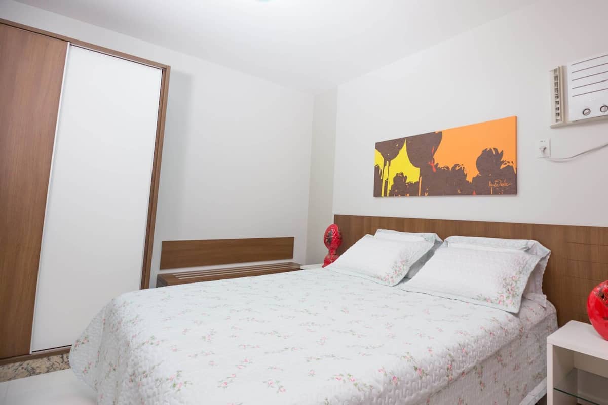 A bedroom with a bed, a wardrobe, a nightstand, and a wall-mounted heater.