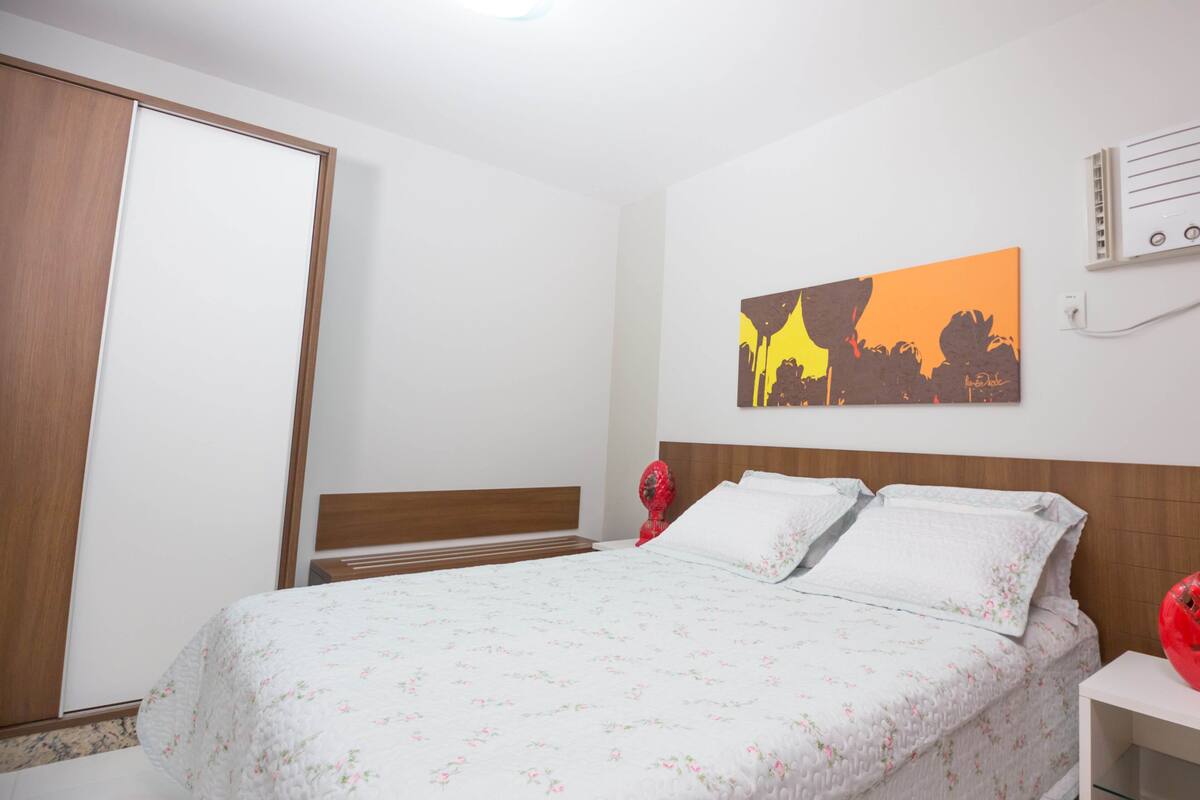 A bedroom with a bed, a wardrobe, a nightstand, and a wall-mounted heater.