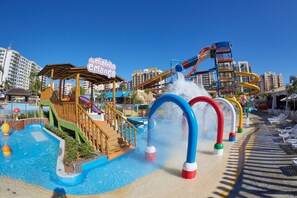 Un parque acuático con un tobogán grande, una piscina y una zona de playa con sillones de descanso.