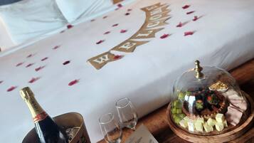Een bed met een 'Welcome' bord, een champagnefles, twee glazen en een dienblad met eten en noten.