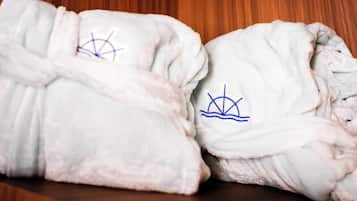 Two white bathrobes with blue embroidery on a wooden shelf.