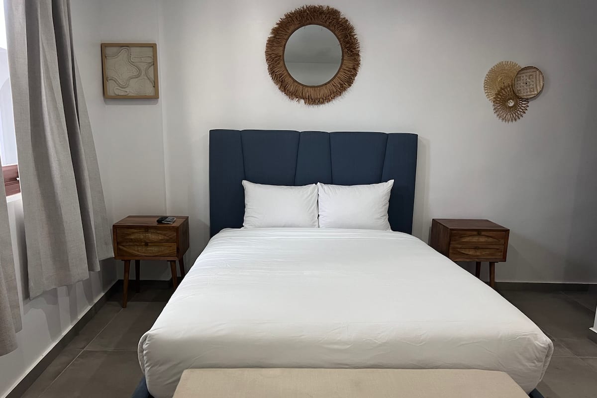 Ein ordentlich eingerichtetes Schlafzimmer mit einem großen Bett, zwei Nachttischen, einer Nachttischlampe, einem Spiegel und einer Wanddekoration.