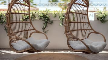 Two wicker swing chairs with cushions, a woven rug, and a white wall with greenery.