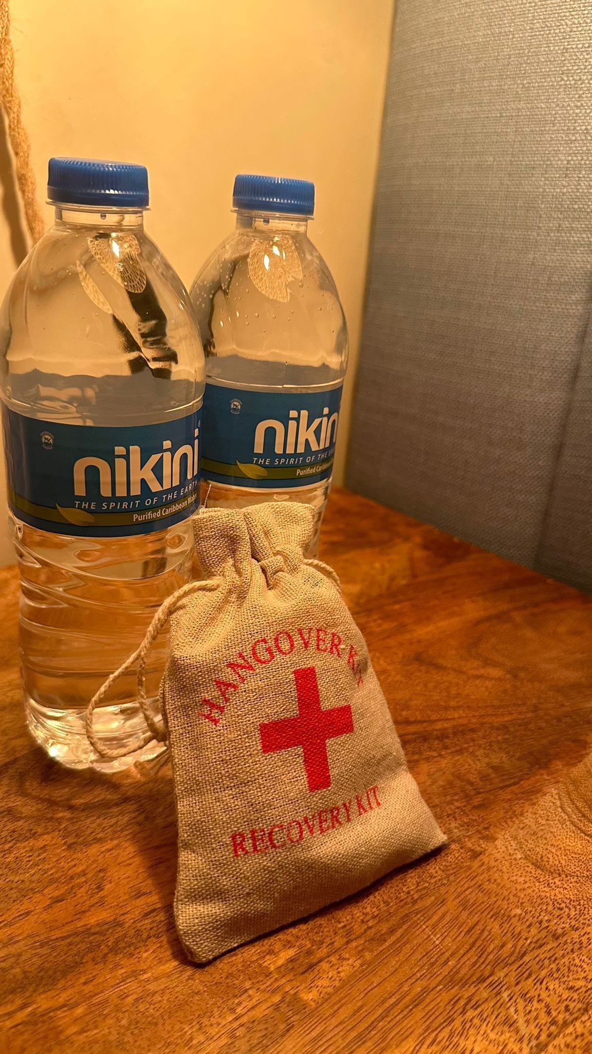 Dos botellas de agua NIKIN y una pequeña bolsa de arpillera con una cruz roja y texto sobre una superficie de madera.