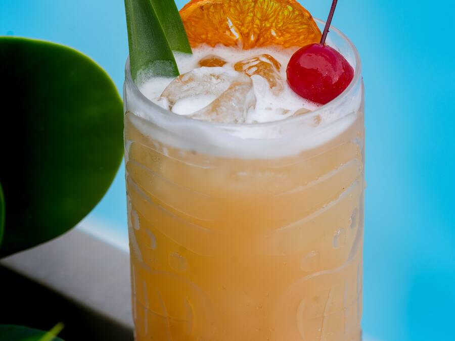 A cocktail with a cherry and an orange slice on a glass.