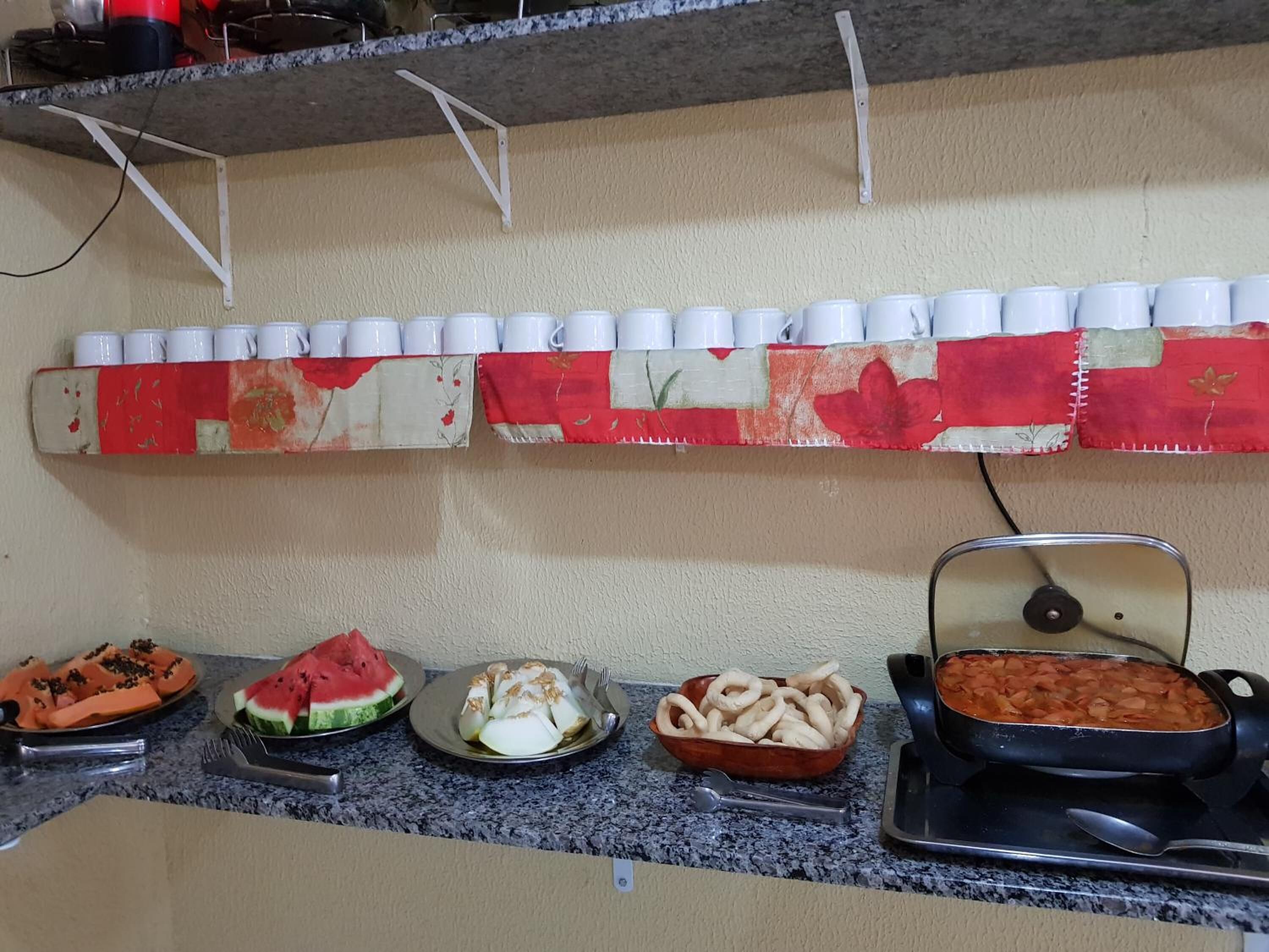Montaje de bufé con diversos alimentos y una fila de vasos blancos en una pared.