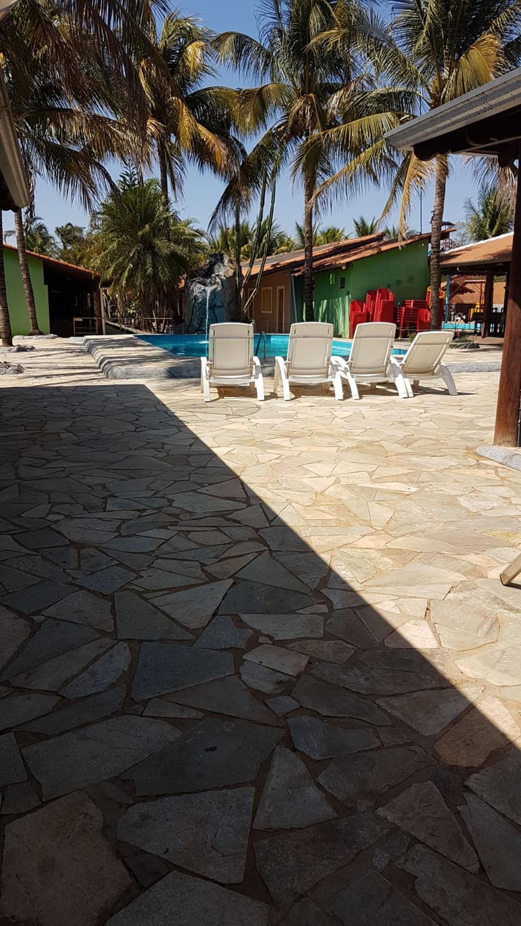 A stone-tiled pool area with lounge chairs, palm trees, and a small waterfall feature.