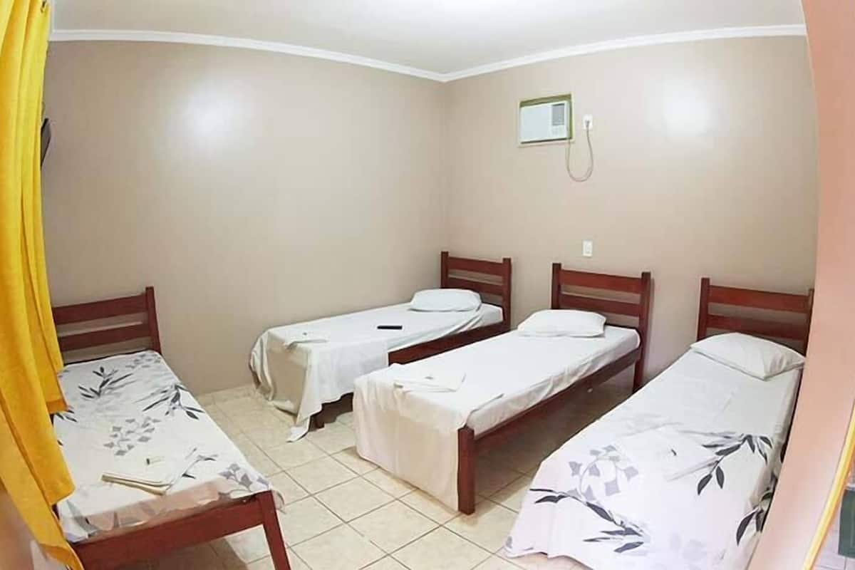 Een kamer met vier eenpersoonsbedden, een klein raam en een badkamer met toilet en douche.